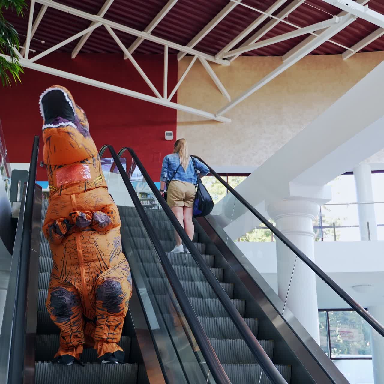 Funny dino costume animator walking in the mall. Orange spotted T-Rex doing shopping