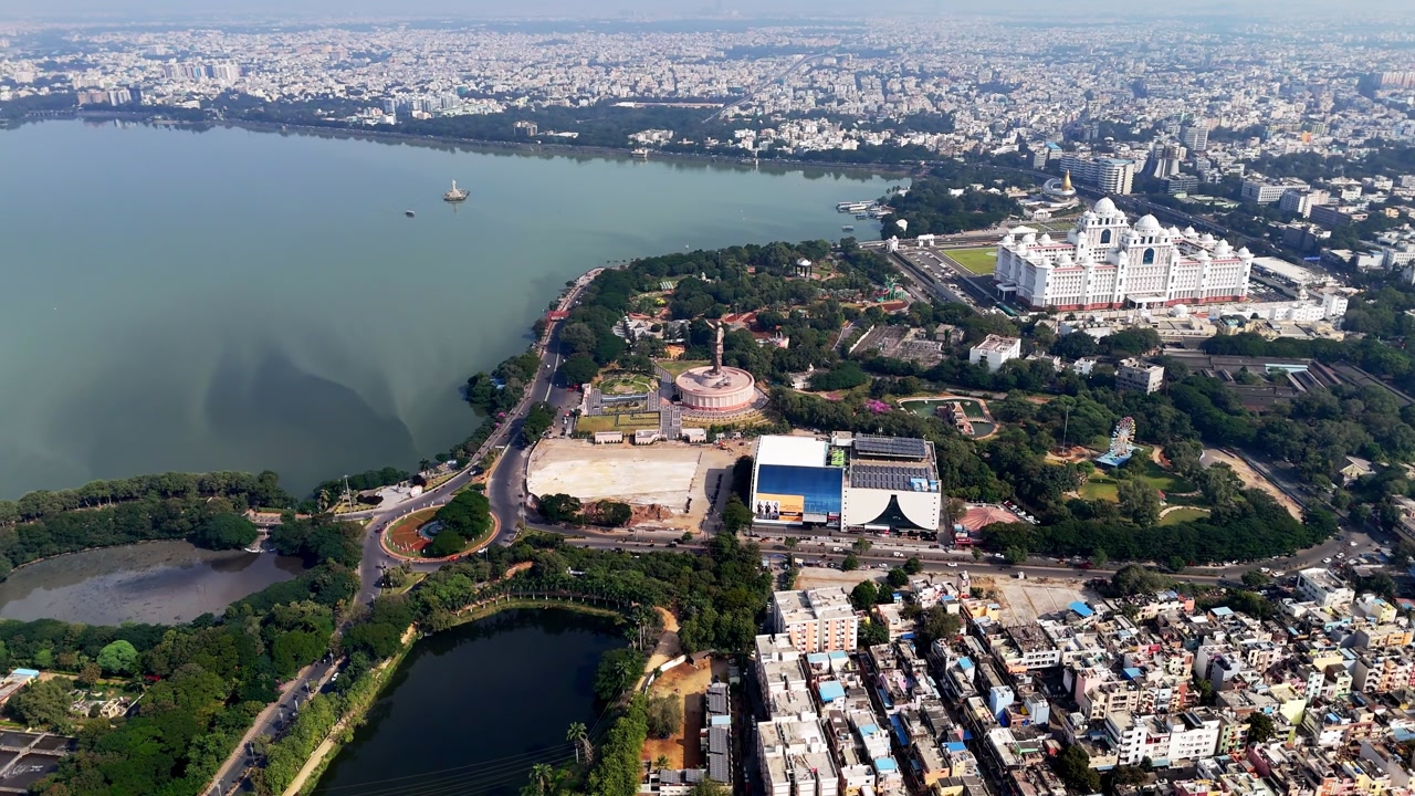 Drone footage capturing Hussain Sagar, nearby landmarks, green spaces, and urban neighborhoods blending into Hyderabad’s expansive skyline.
