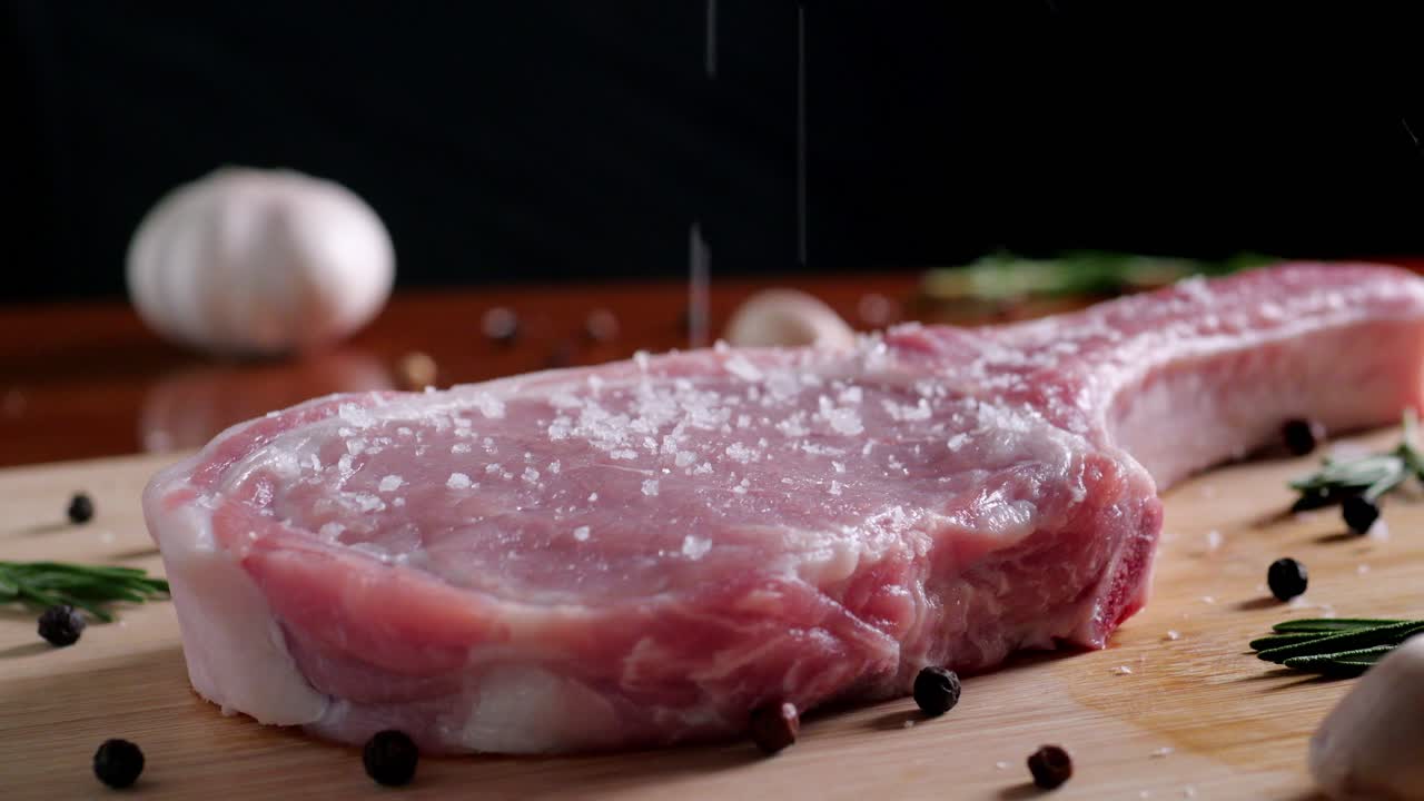 chef estaciones bife crudo con sal en una tabla de corte de madera, cámara lenta, primer plano