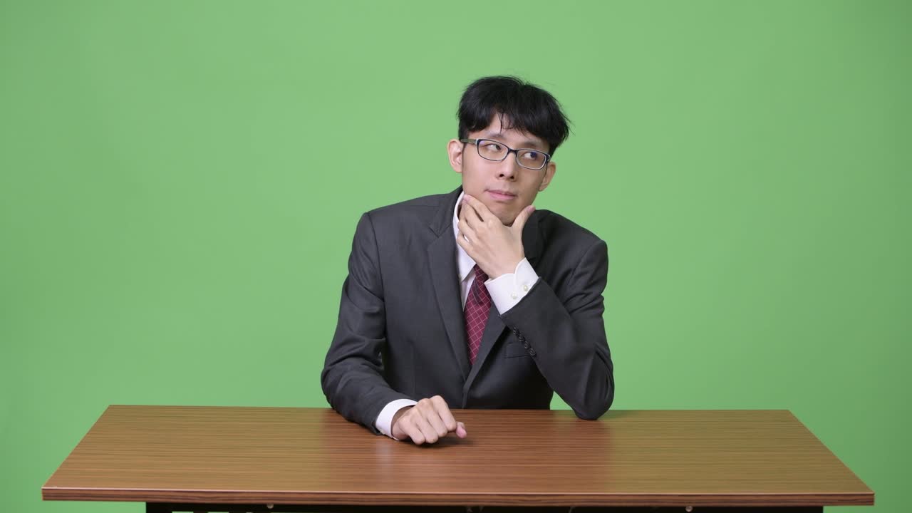 若いアジア人ビジネスマンが上を見上げながら考えている