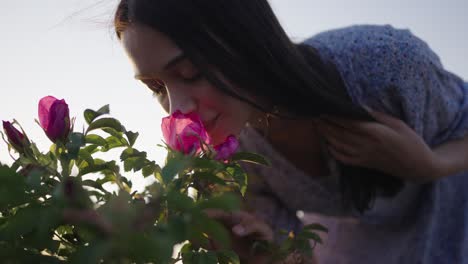 mujer con vestido floral púrpura sostiene el cabello inclinado hacia abajo para oler las flores al atardecer