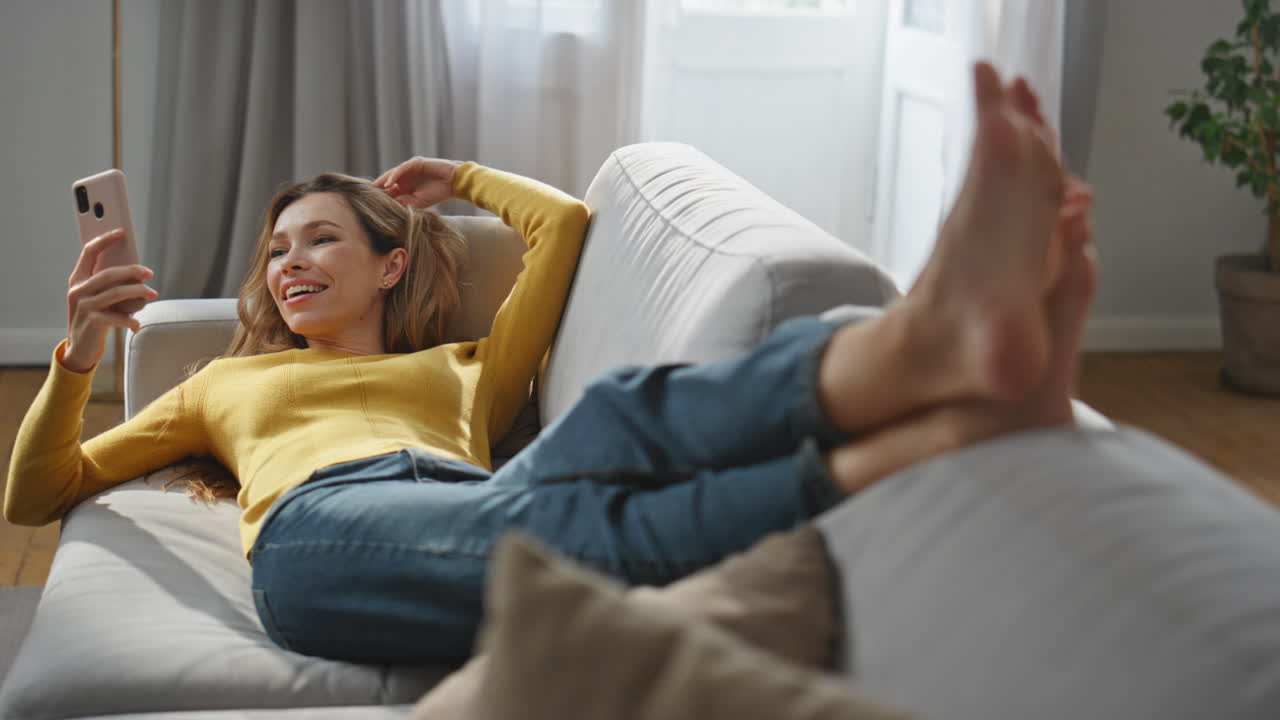Happy lady video calling cellphone chilling at home. Woman making selfie laying