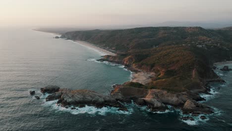 aerial backwards shot of beautiful punta cometa viewpoint and mazunte beach with coastline in background during foggy sunset in mexico