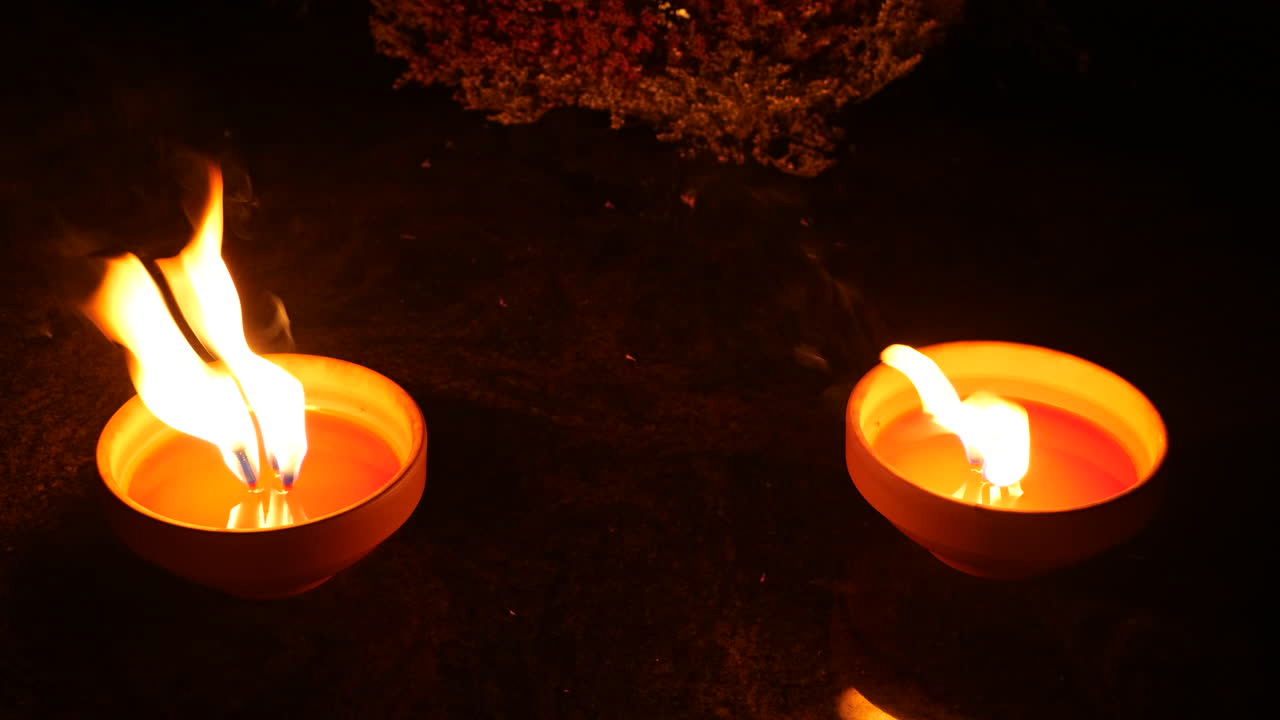 Grave wax candles burning at night with flame and smoke in strong wind on cemetery tombstone.