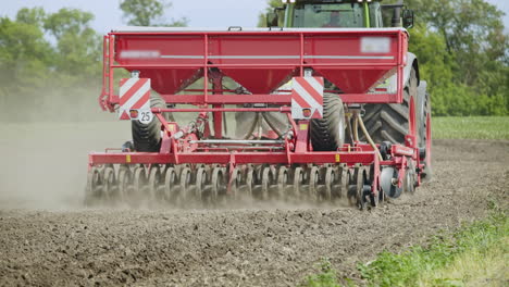 agricultural tractor with trailer seeder working on plowed field. rural farming