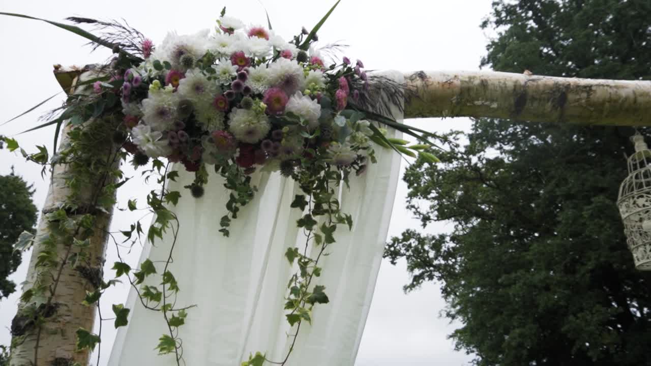 Panoramica ravvicinata di una decorazione nuziale con fiori e gabbie per uccelli su un arco di betulla nel bosco.