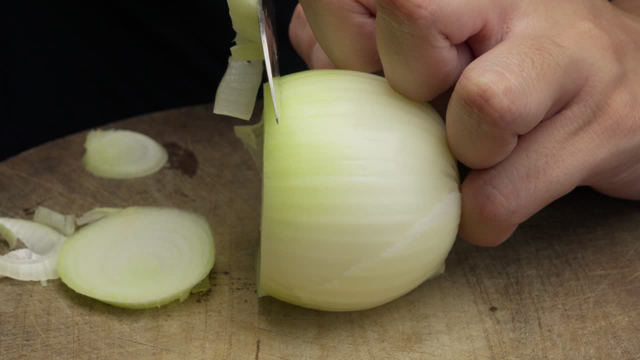 Primer plano de cebolla siendo cortada en una tabla con un cuchillo afilado.