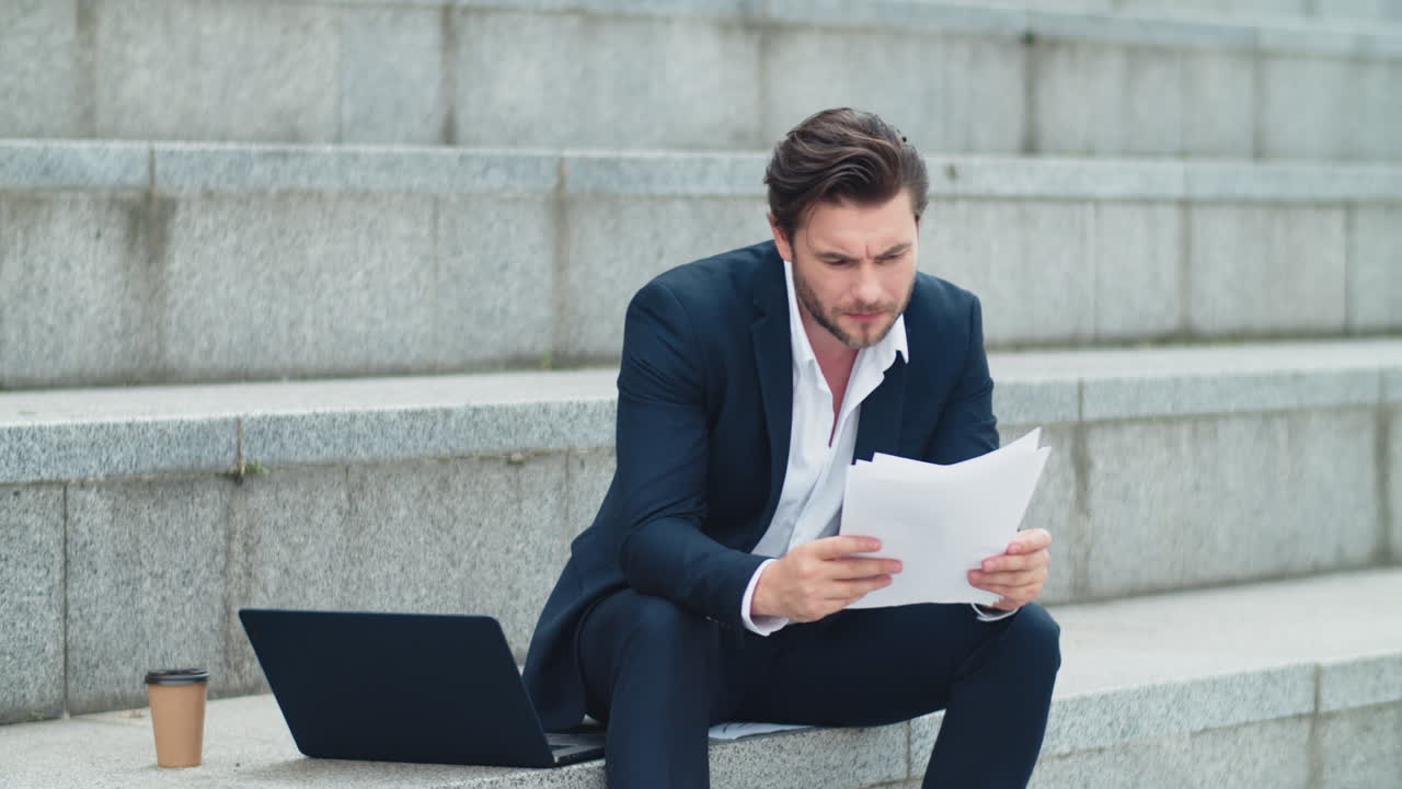 Businessman reading business papers on street. Worried man sitting on stairs
