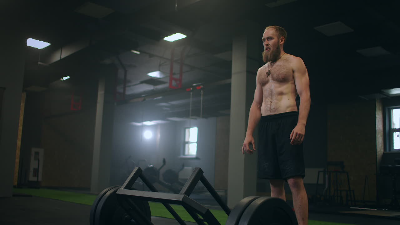 피곤한 남자가 무게를 들어 올린 후 휴식을 취합니다. 빌나이 운동은 데드리프트입니다. 훈련 전에 집중력을 준비하고 조정합니다. 체육관에서 증기와 함께 운동 선수의 기분과 무거운 호흡