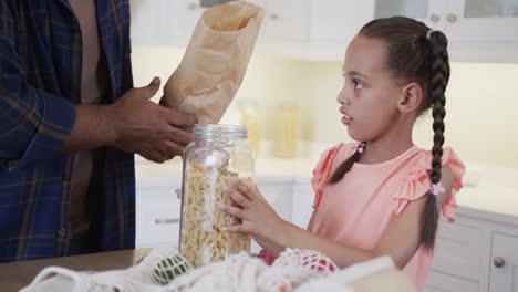 Happy biracial father and daughter unpacking shopping in kitchen, slow motion