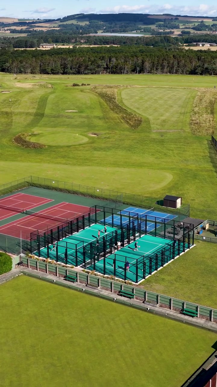 Dron sobrevuela casas junto a la playa, calles del pueblo, canchas de tenis y un extenso campo de golf verde.