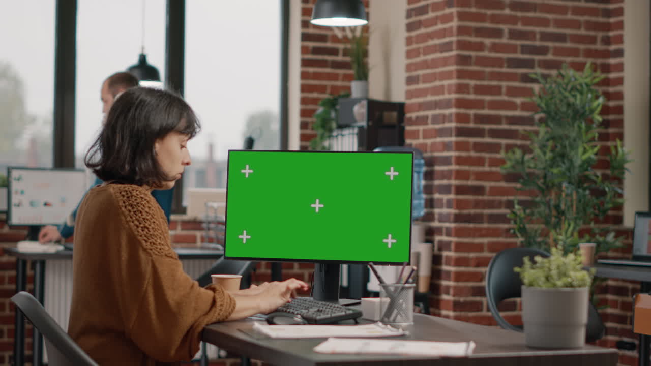 Woman working on computer with green screen in office