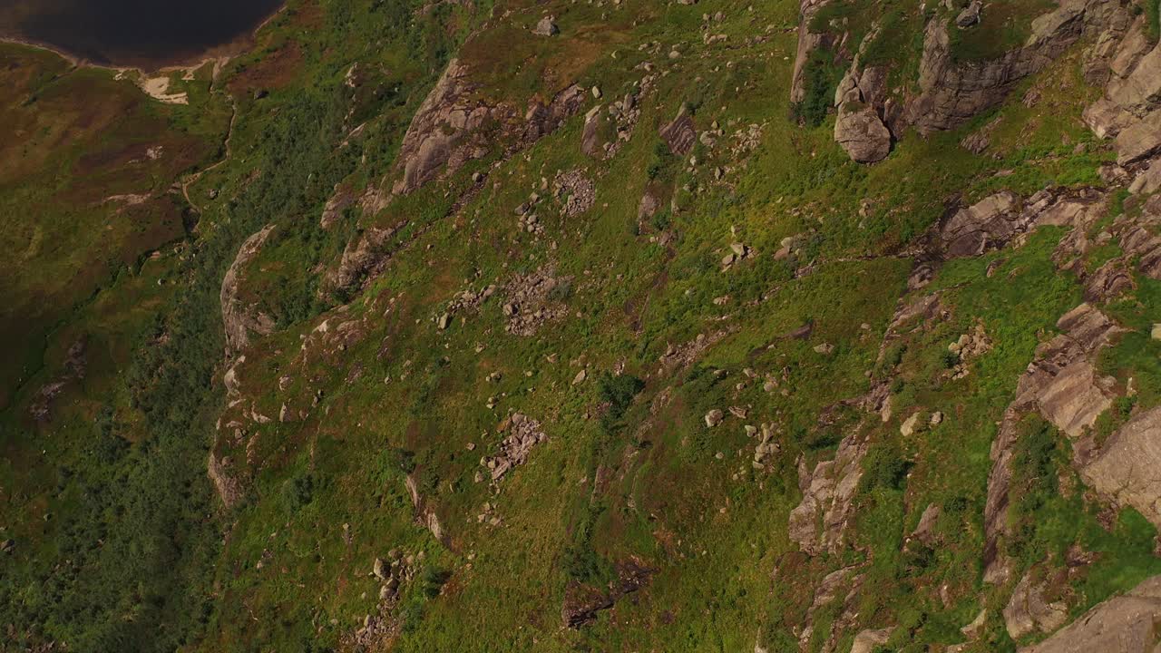Aerial shot of lush green hills in Norway, with rocky terrain and a distant lake