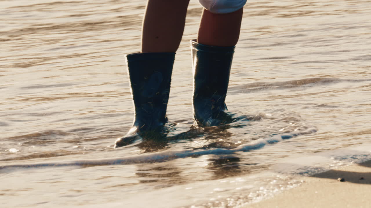 Close up of a child's legs wearing waterproof boots while standing in shallow sea water