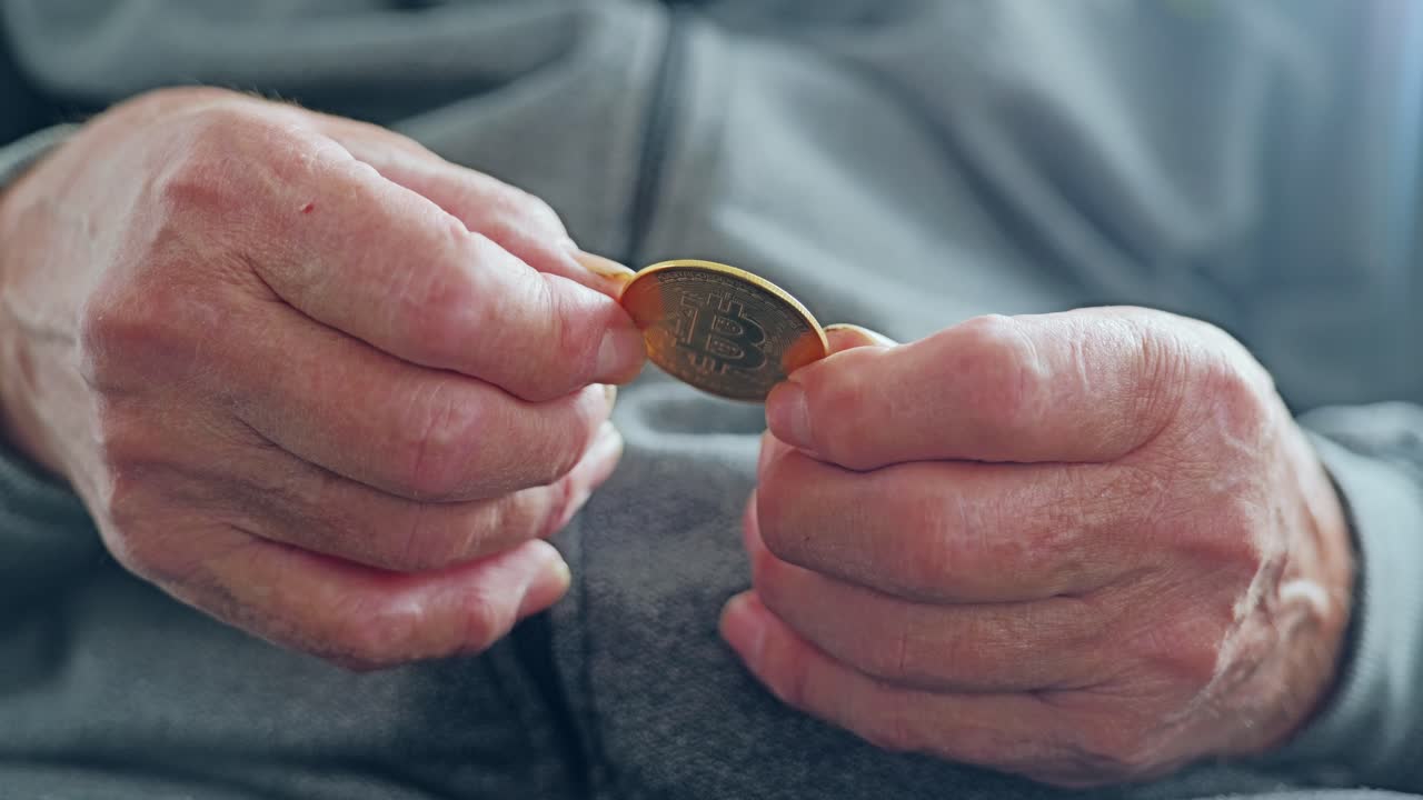 Primer plano de las manos de un hombre mayor sosteniendo una moneda de bitcoin como símbolo de arma financiera