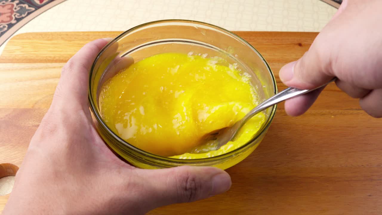 Primer plano de una mezcla de huevo removida en un cuenco, mostrando una textura suave y dorada para la preparación de la comida. Ideal para recetas, desayunos, repostería y contenido gastronómico.
