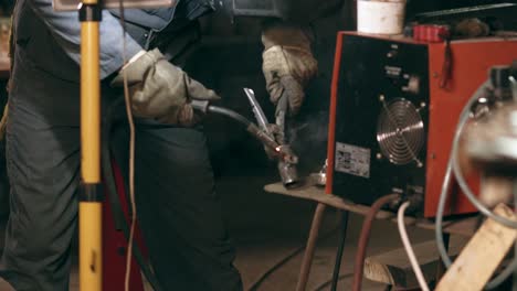 male worker in protective gloves welds two metal pieces together at mechanical hangar