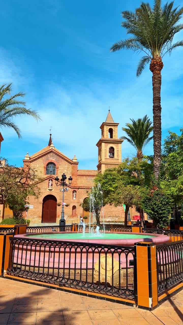 Cartagena, Hiszpania, 8 sierpnia 2025: Kościół Santa Maria de Gracia i fontanna w Kartagenie. Widok historycznego ceglanego kościoła i centralnej, okrągłej fontanny na słonecznym placu w Kartagenie w Hiszpanii.