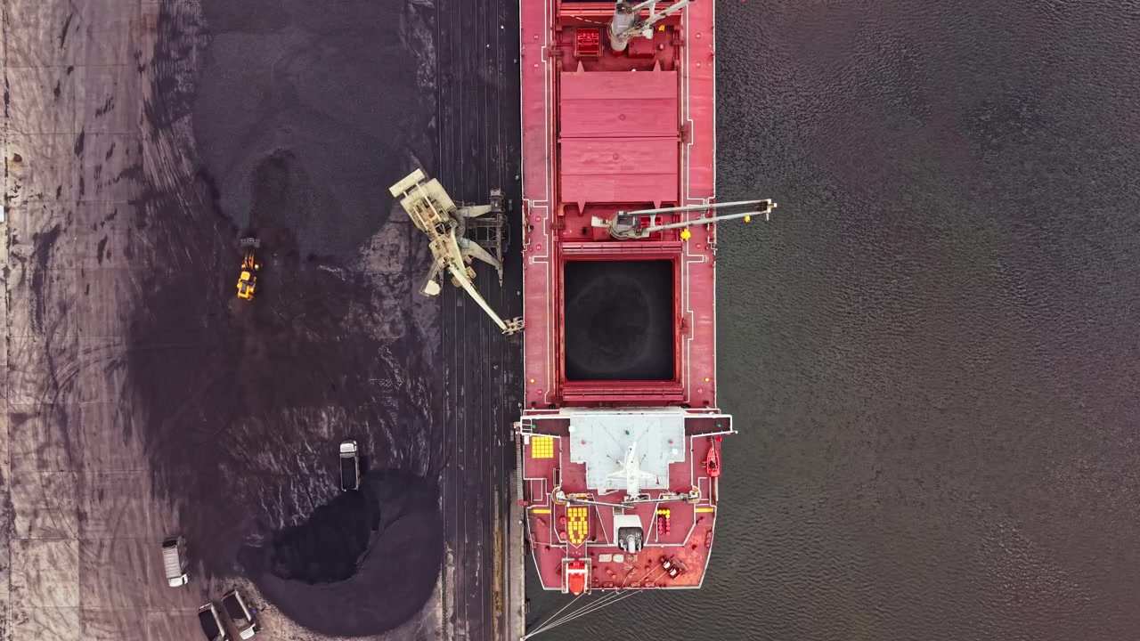Nave da carico che scarica materiale in una grande area portuale durante le ore diurne con macchinari che lavorano attivamente sul molo.