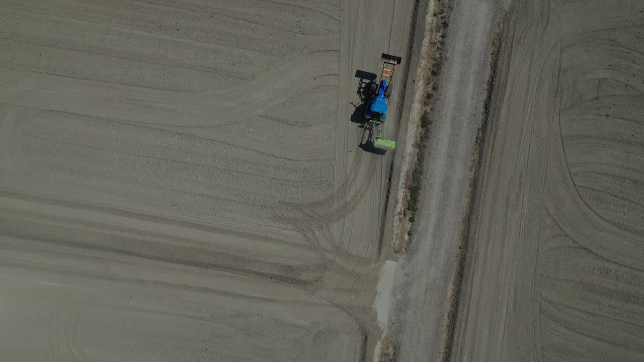 A tractor working in gelsa zaragoza on dry, flat farmland during the day, aerial view