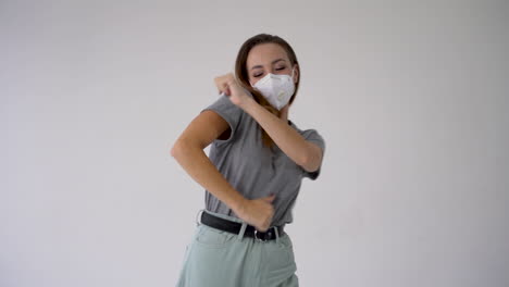 el final de la cuarentena de covid-19. mujer joven y alegre bailando y usando máscara médica en fondo blanco.