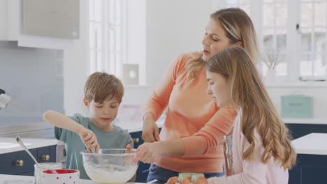 mother with two children in kitchen at home having fun baking cakes together