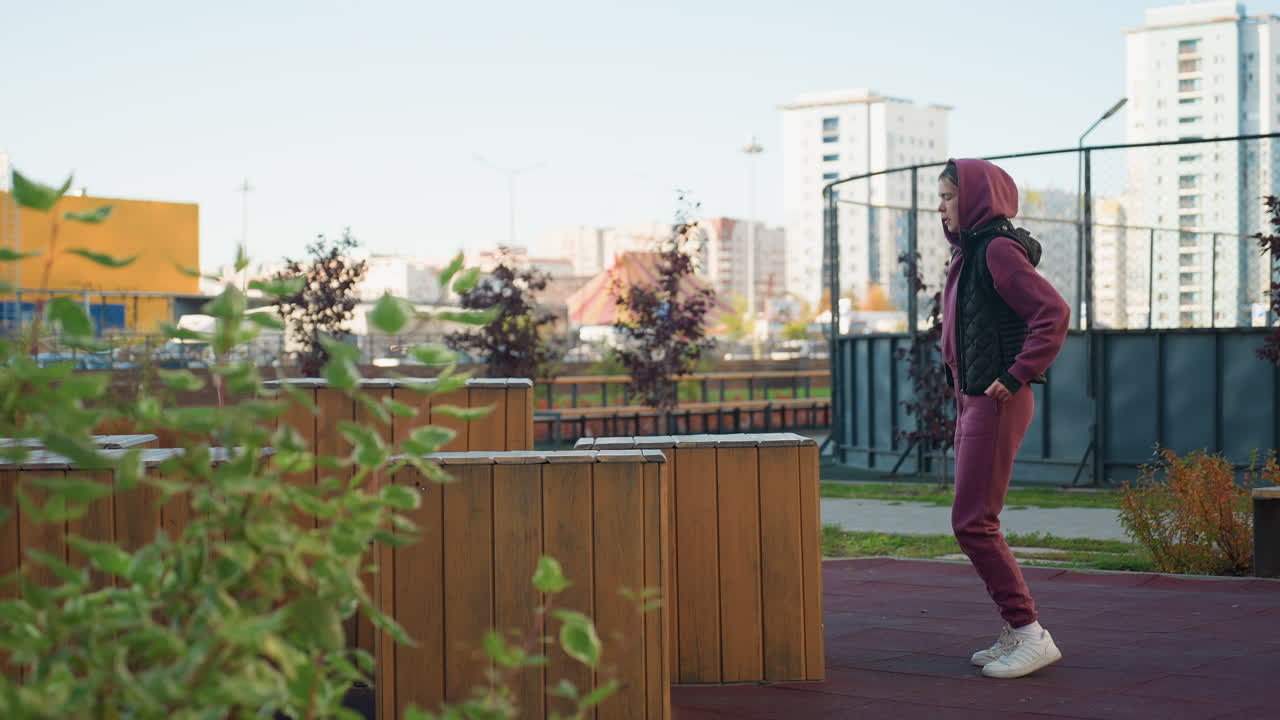 Strength trainer jumping up in sneakers and hoodie on wooden bench in urban park, showcasing explosive jump power and agility, dynamic movement, focus and energy during autumn outdoor fitness routine