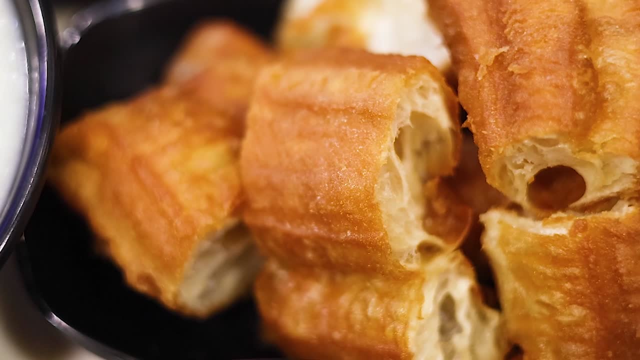 Close-up of golden brown dough sticks served in a black bowl, showcasing their crispy texture.