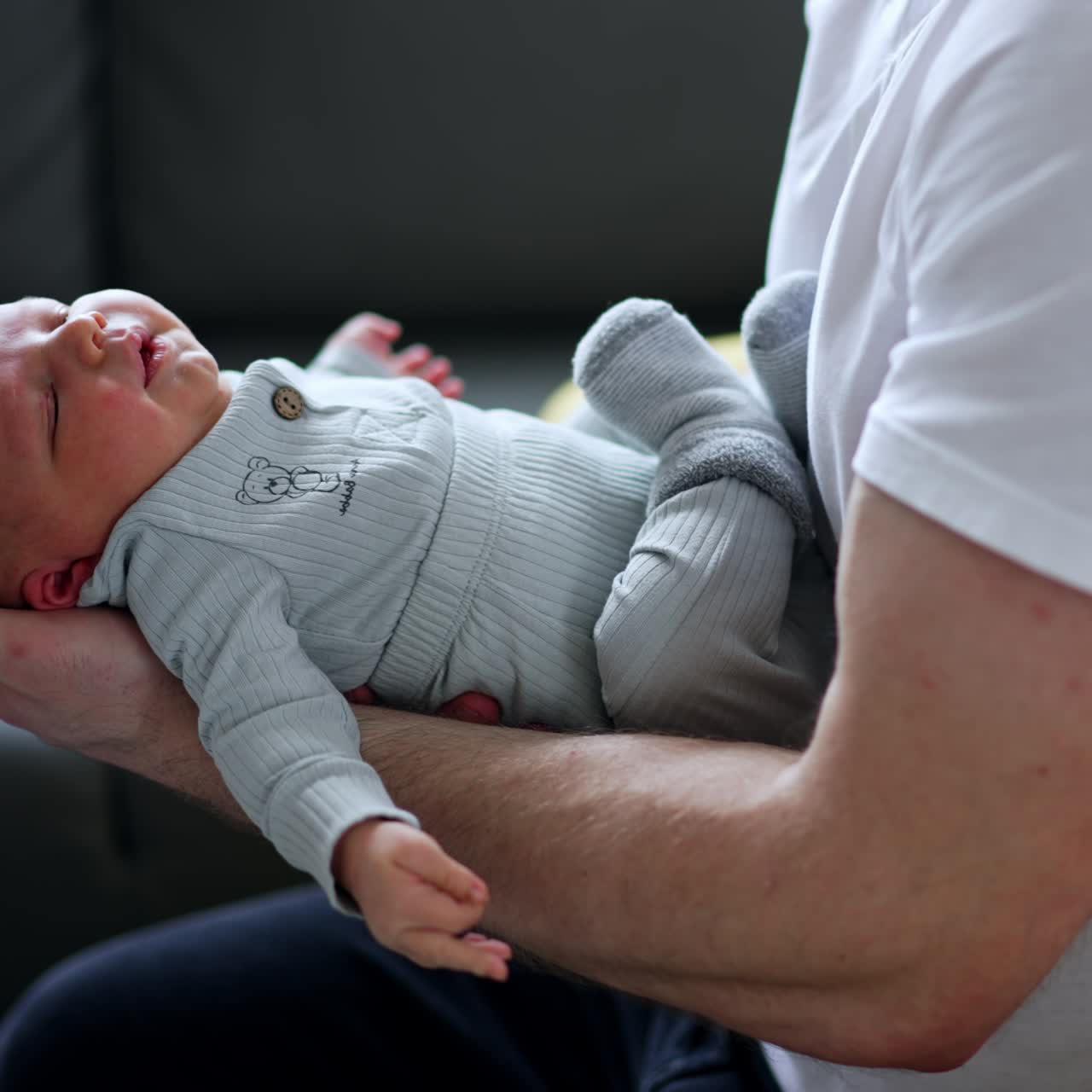 Adorable newborn baby boy in blue romper. Infant is dandled by the father. Child sleeping in dad's arms. Close up