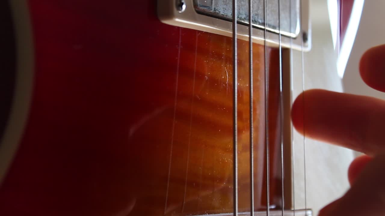 Fingers picking the strings of a Les Paul electric guitar in cherry sunburst