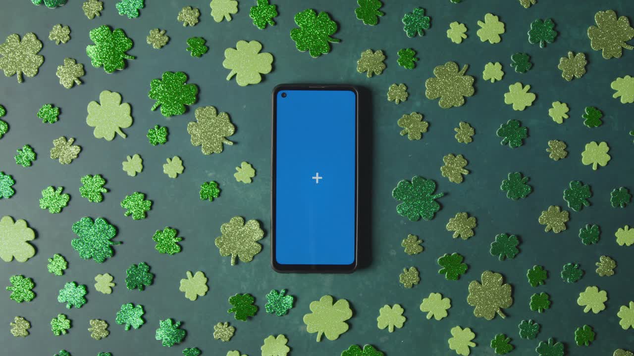 Overhead Studio Shot Of Green Shamrock Shapes Surrounding Blue Screen Mobile Phone To Celebrate St Patricks Day