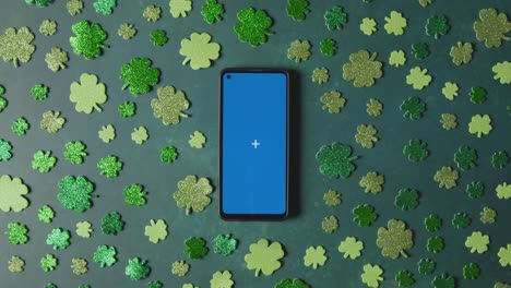 Foto-De-Estudio-Superior-De-Formas-De-Trébol-Verde-Que-Rodean-El-Teléfono-Móvil-De-Pantalla-Azul-Para-Celebrar-El-Día-De-San-Patricio