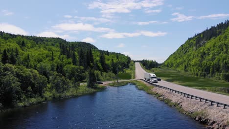 Ein-Weißer-Sattelschlepper-Fährt-Tagsüber-In-Ontario,-Kanada,-Eine-Autobahn-Hinunter,-Die-Von-Wäldern-Und-Bergen-Umgeben-Ist,-Neben-Einem-See