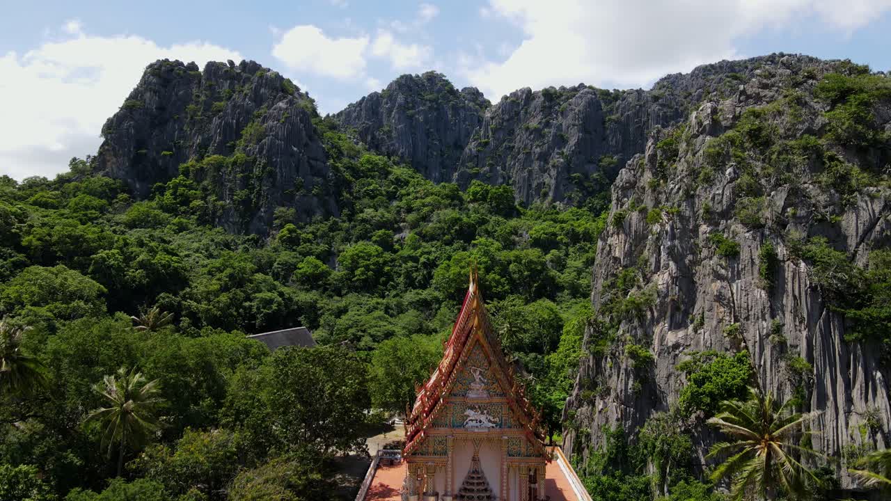 Ascending aerial footage of the Wat Khao Daeng with limestone mountains and a forest in Khao Sam Roi Yot National Park, Phrachuap Khiri Khan, Thailand