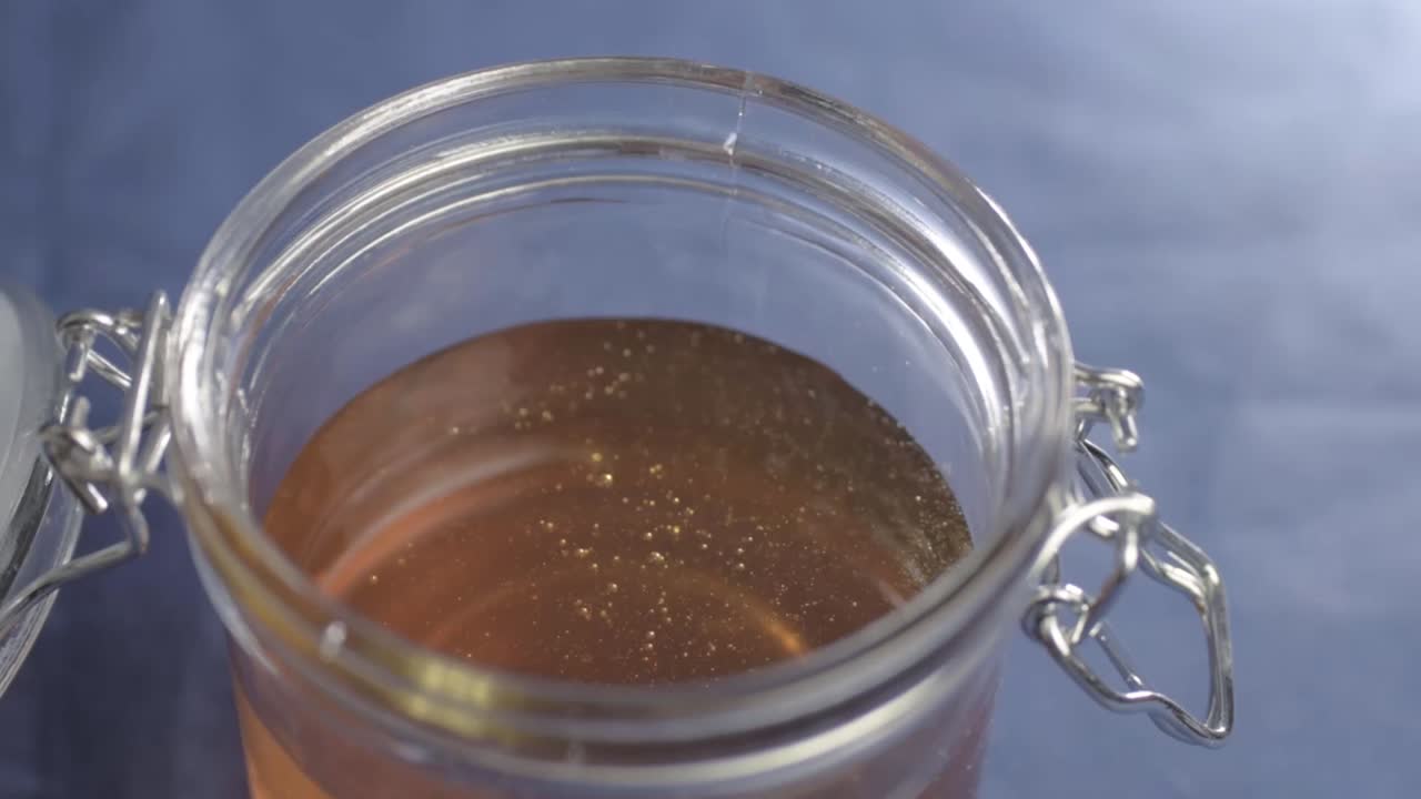 Pouring golden runny honey into a glass jar overhead shot