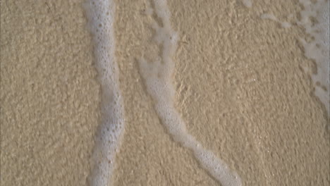 slow motion close up of the water coming in the beach with foam an bubbles with the waves in calm tranquil manner