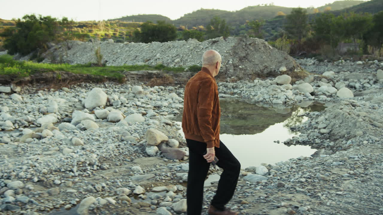 Elderly Man Walking Along the Edge of a Riverbed