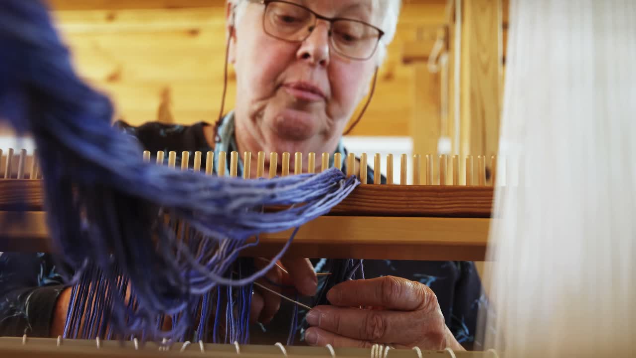 vista a basso angolo di una vecchia donna caucasica anziana che prepara e si siede alla macchina a telaio a mano in un workshop