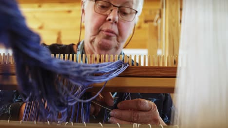 low angle view of old caucasian senior woman preparing and sitting at hand loom machine in a worksho