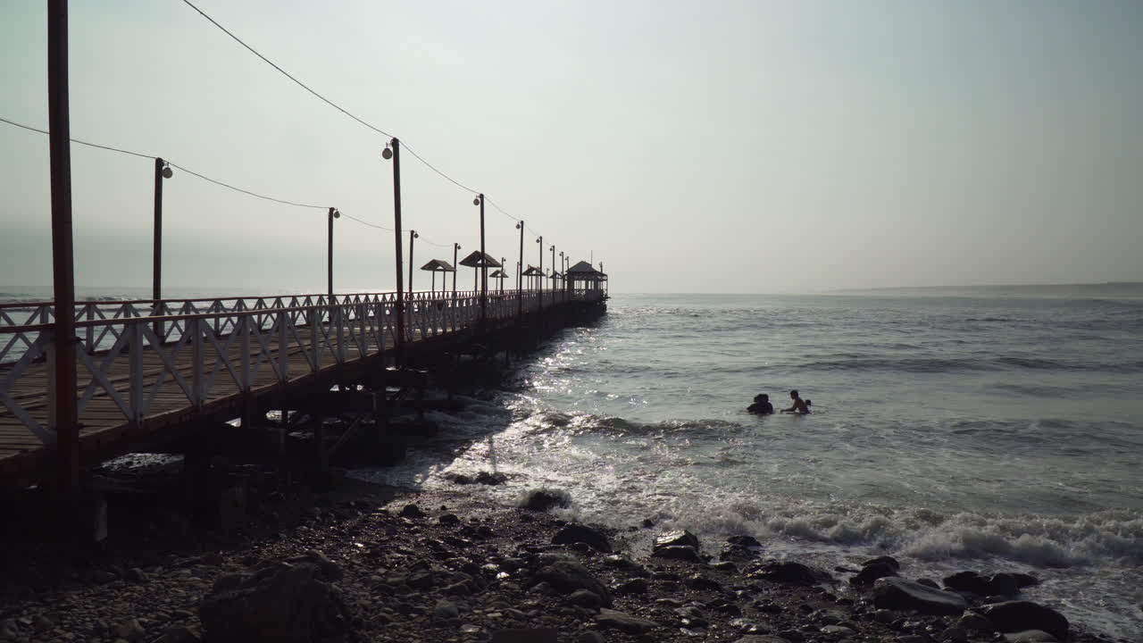 People Swimming in the Ocean near a Pier