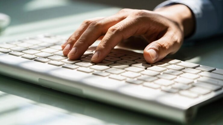 Typing right hand hovering then pressing keys at desk, showing white keyboard cuff for office work