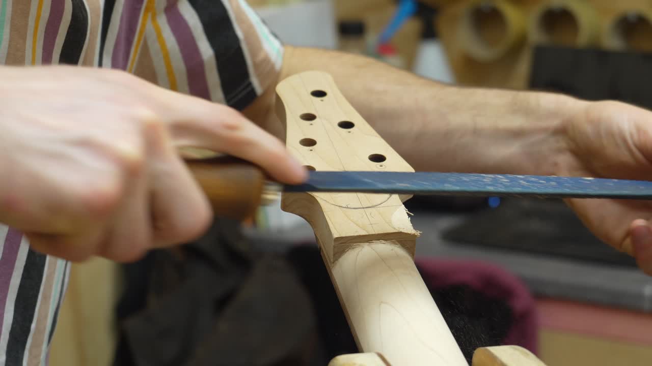 Luthier's hands filing back side on guitar's neck at workshop - close-up