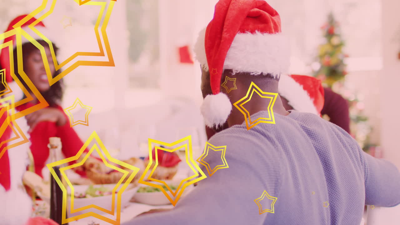 Animasi bintang-bintang berjatuhan di atas keluarga Afrika-Amerika yang bahagia mengenakan topi santa dan sedang makan malam