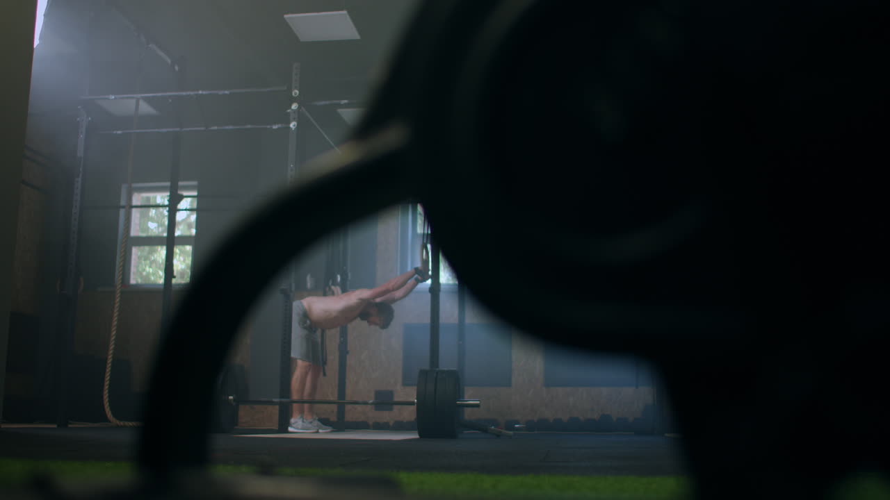 молодой атлетический белый мужчина переодевается, надевает ремни для подъема тяжестей в раздевалке перед тренировкой, замедленное движение. привязывает руки к штангерам с фитнес-ремнями.