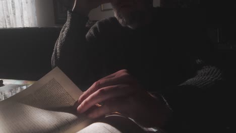 nonchalant bearded man in dimly lit shadows idly turning book pages medium shot