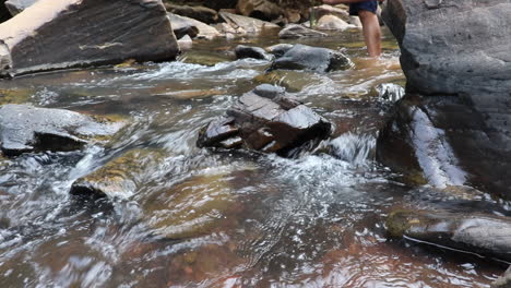 low pov shot of stones on riverbed, mans legs appearing in background