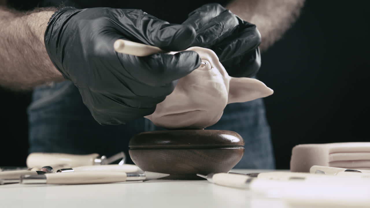 Artist models a plasticine puppet head's eye bulb with a needle tool