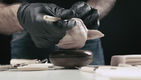 artist models a plasticine puppet head's eye bulb with a needle tool