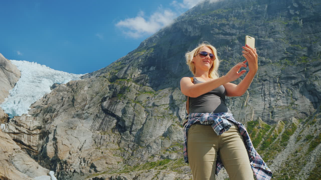 una mujer atractiva se toma una foto contra el fondo de las montañas y el glaci