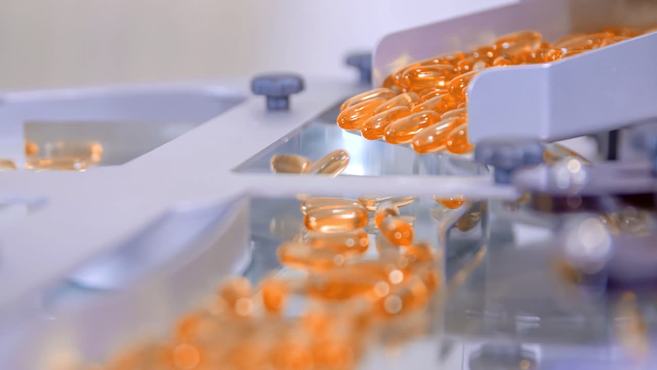 Extreme closeup of orange gel pills falling into a machine during its production